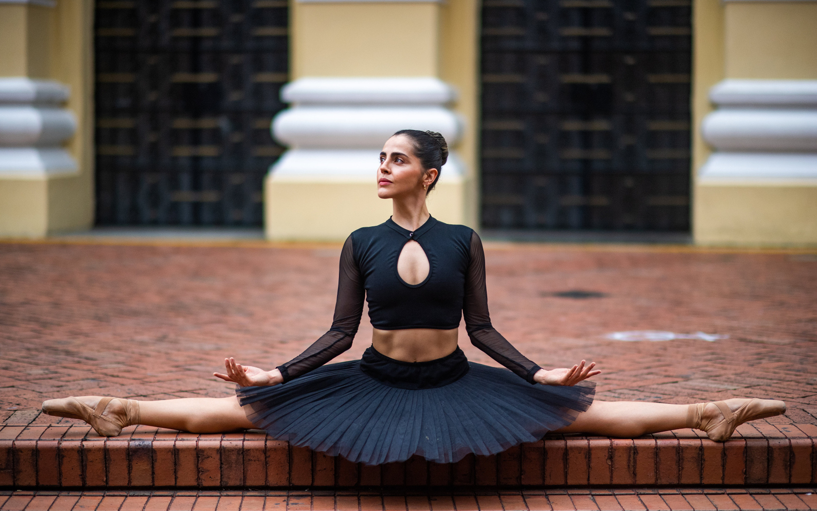 Девушка балерина в черном наряде сидит на шпагате