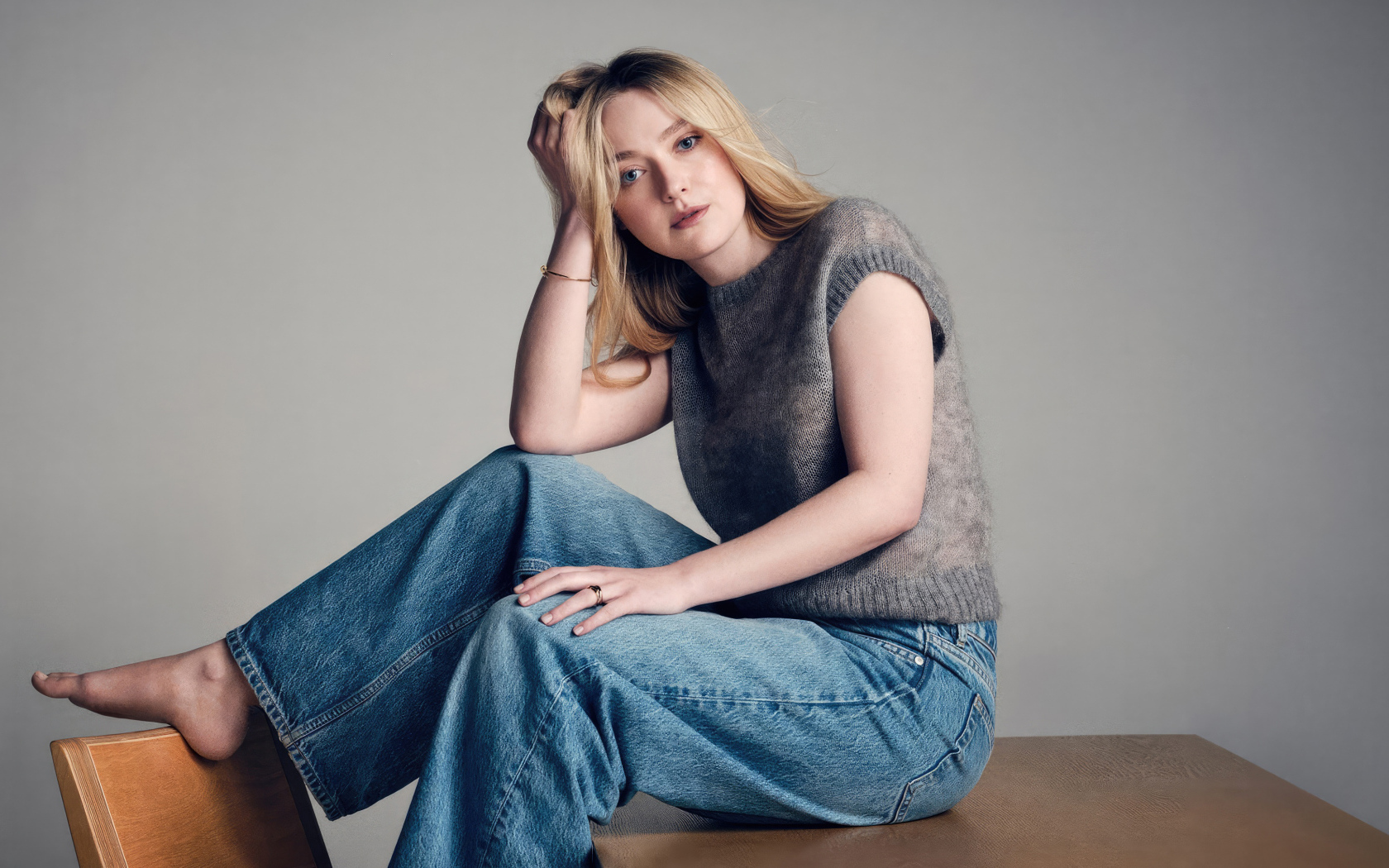 Актриса Дакота Фэннинг в джинсах сидит на столе