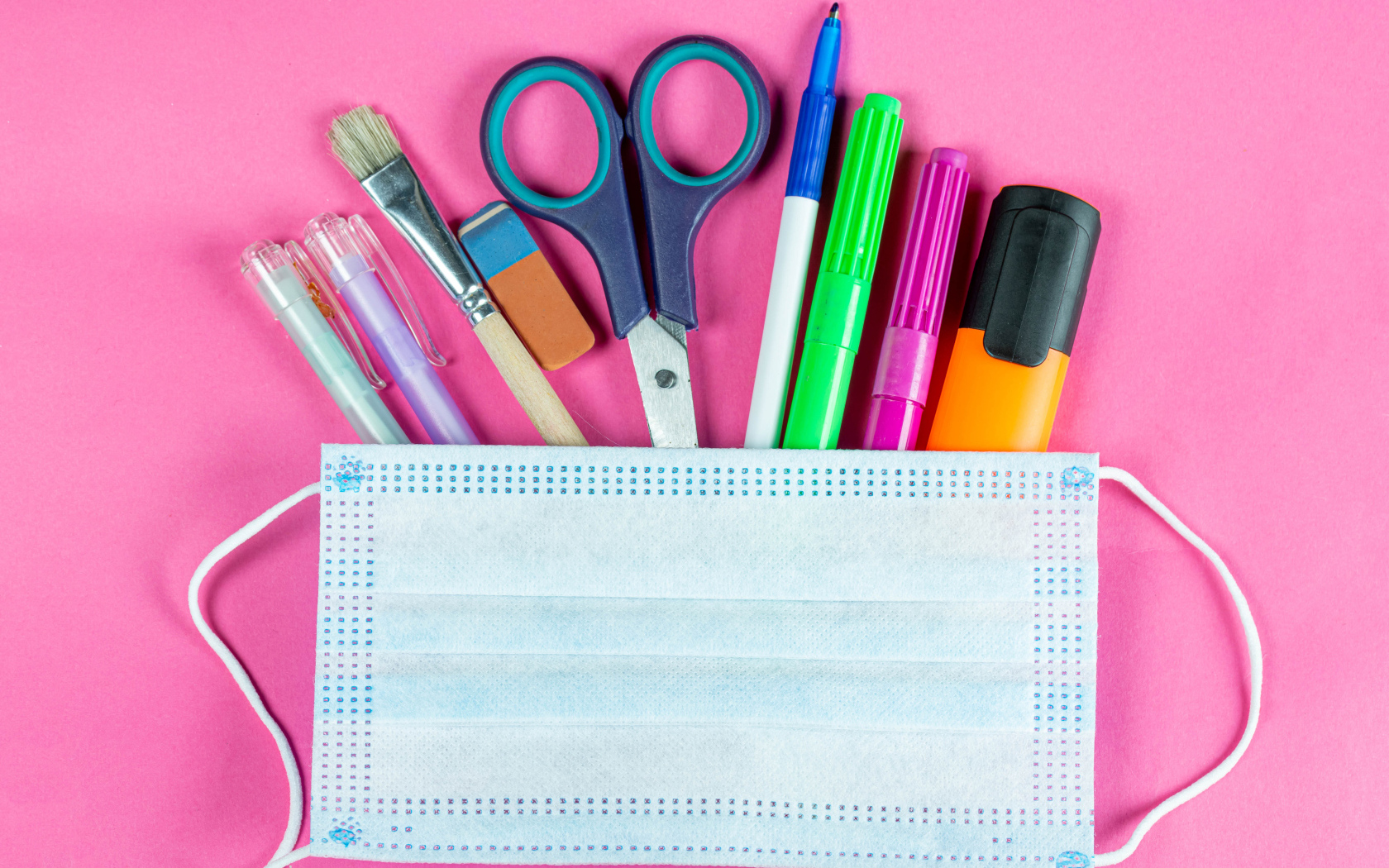Канцелярские предметы и медицинская маска на розовом фоне
