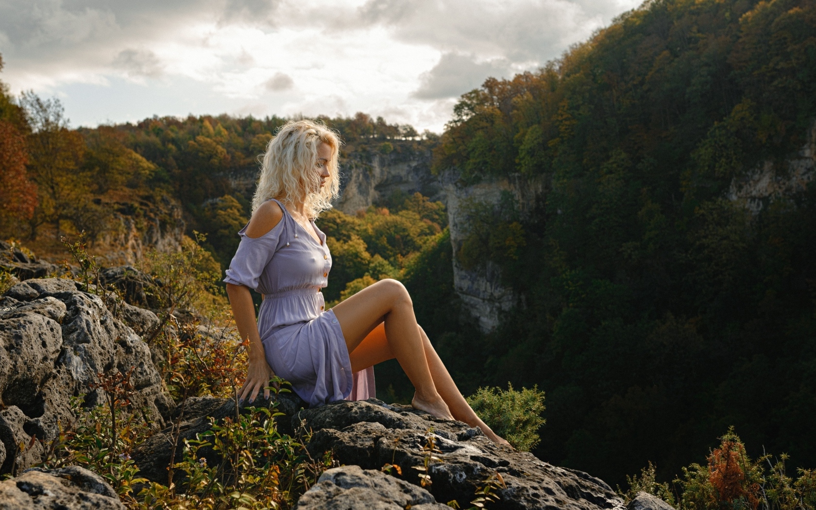 Красивая длинноногая блондинка сидит на краю скалы