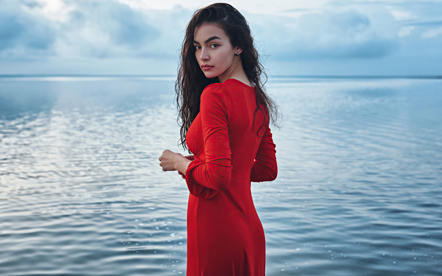 Милая девушка в красном платье стоит у воды