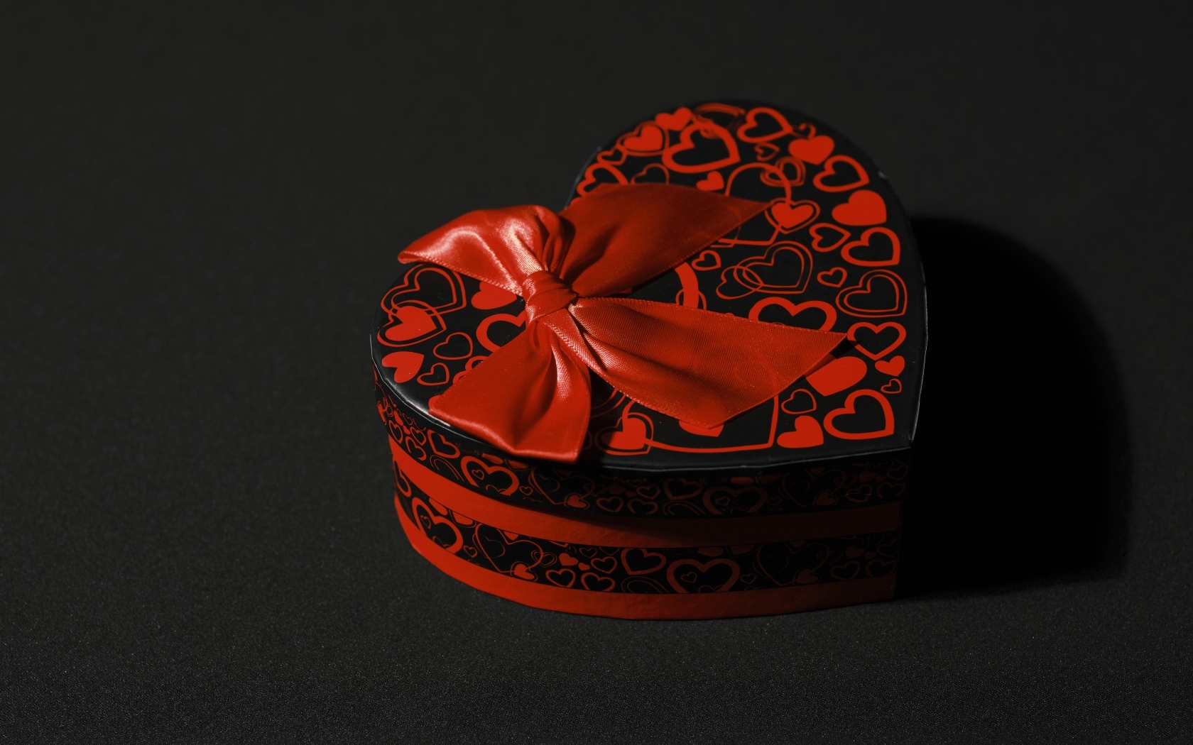 Шкатулка в форме сердца с красным бантом на черном фоне