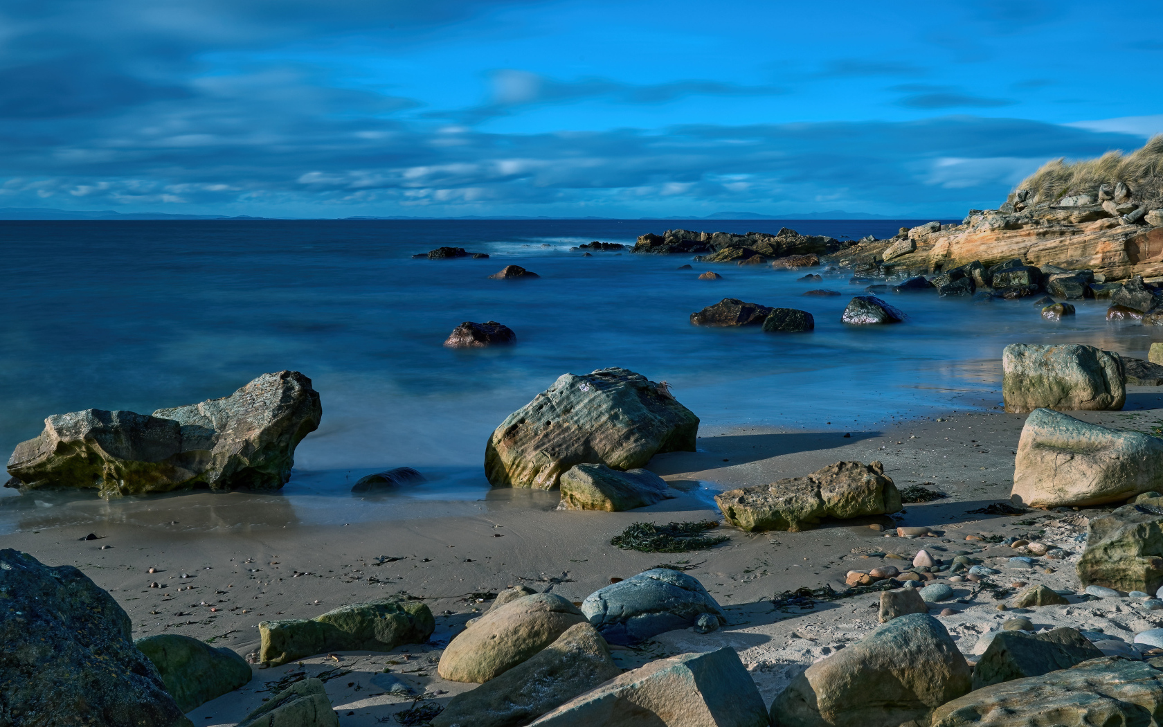 Большие камни на мокром песке у спокойного моря