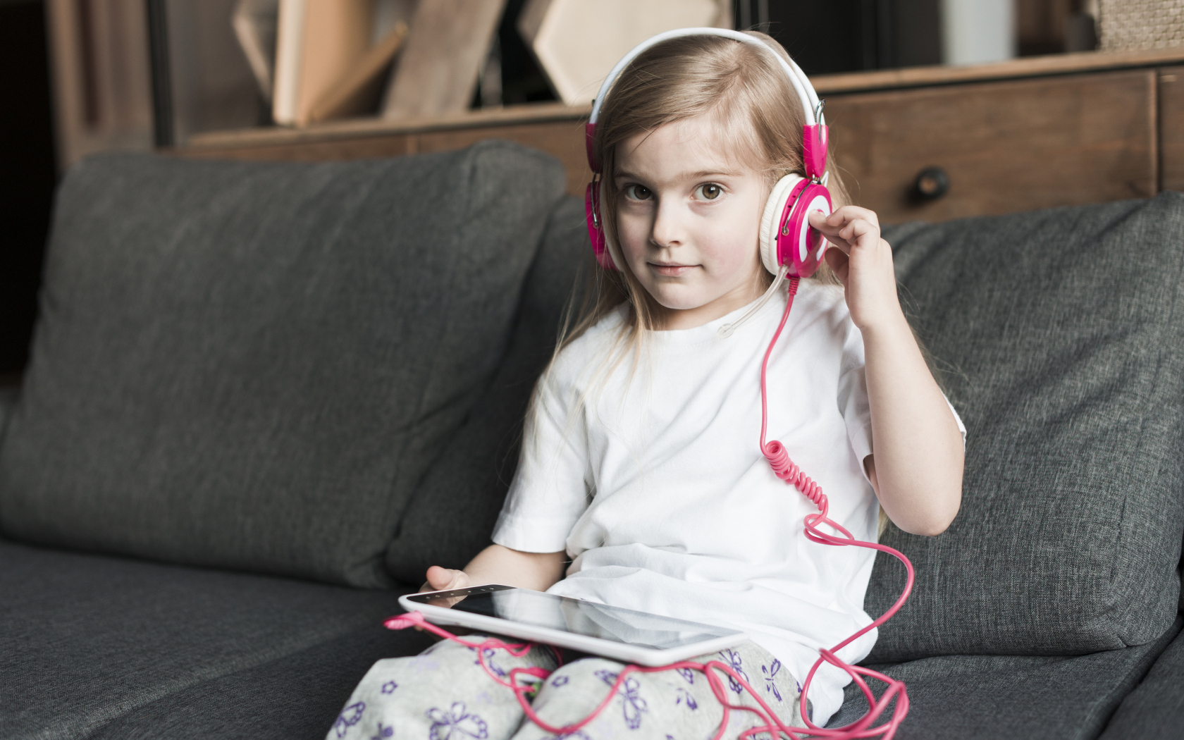 Девочка в наушниках сидит на диване