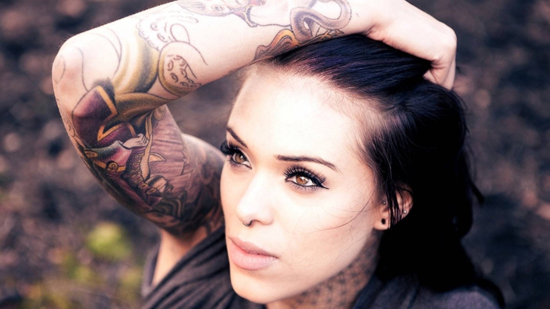 Девушка брюнетка с пирсингом в носу и татуировкой на руке