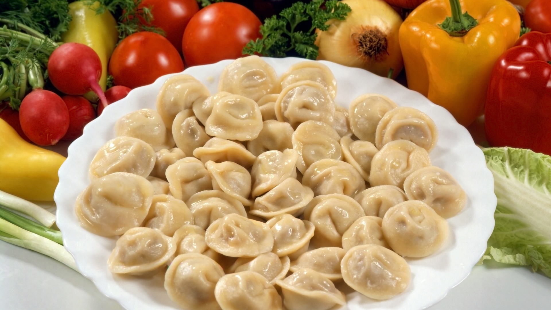 Пельмени на тарелке среди овощей