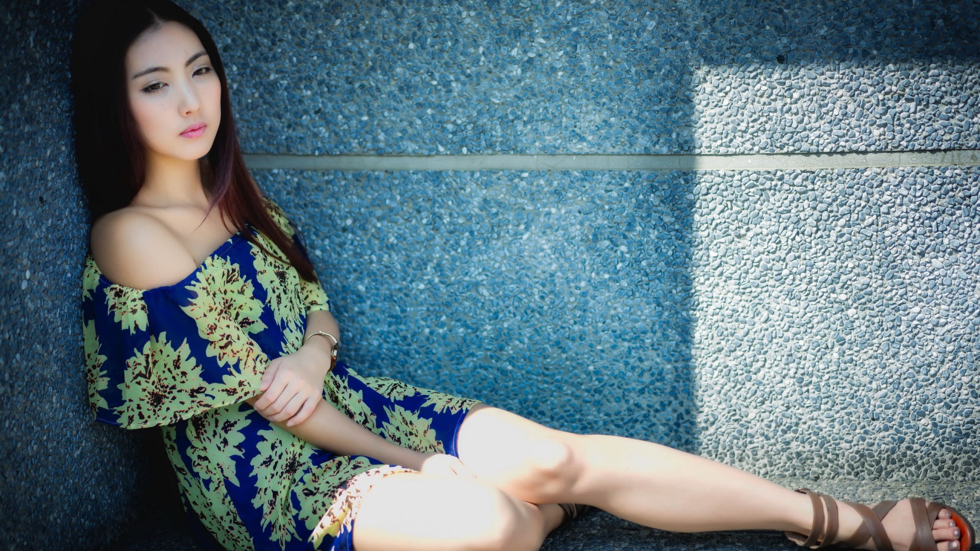 Девушка сидит в тени у гранитной стены