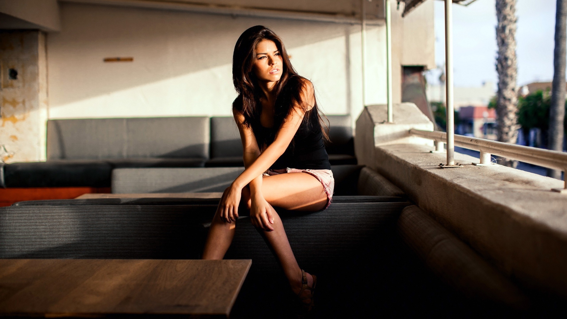Брюнетка сидит на спинке дивана и смотрит в окно