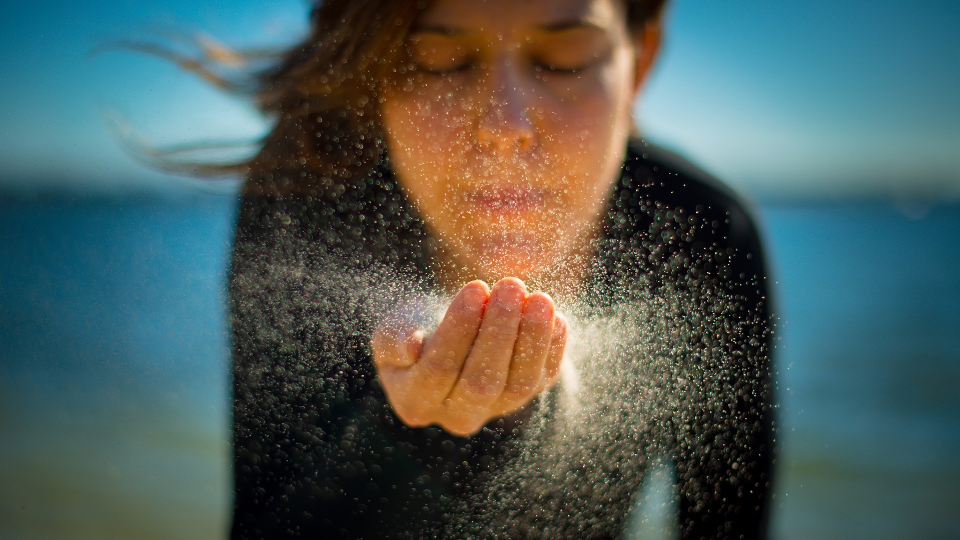 Девушка сдувает песок с руки