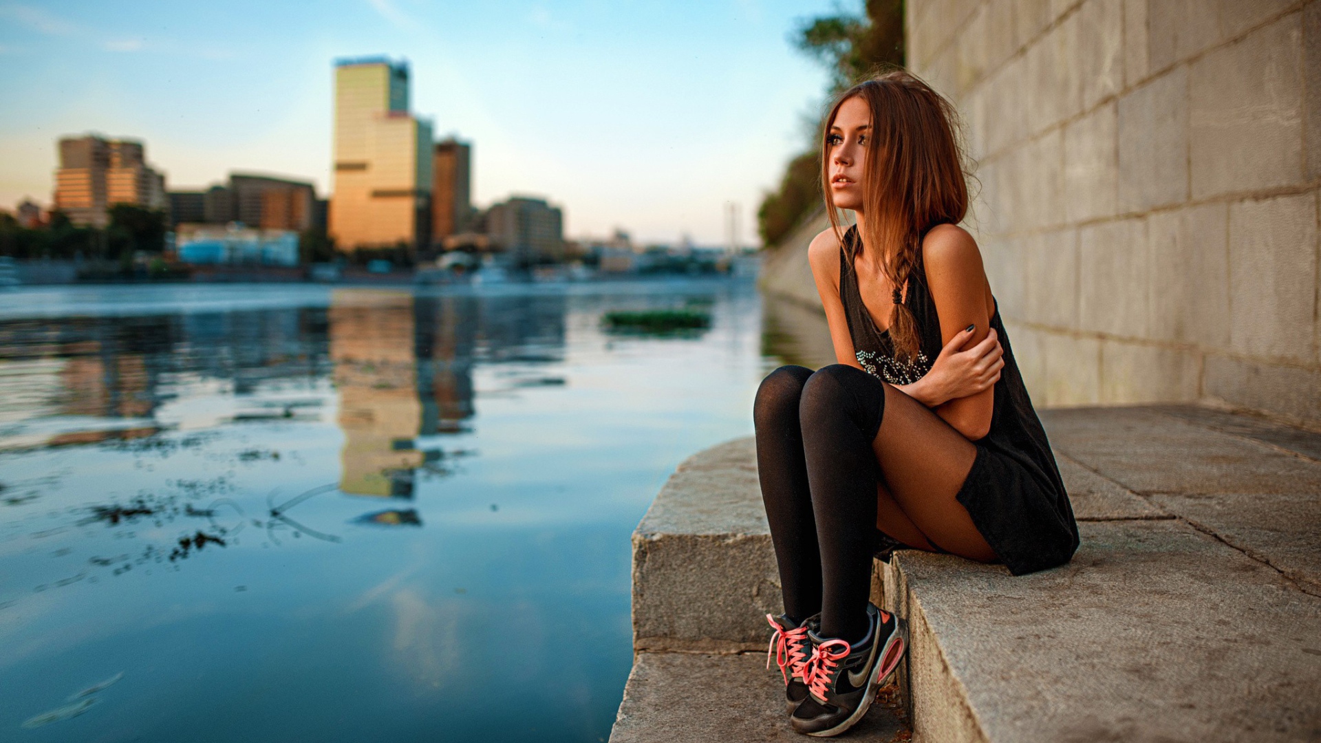 Девушка в кедах сидит на набережной