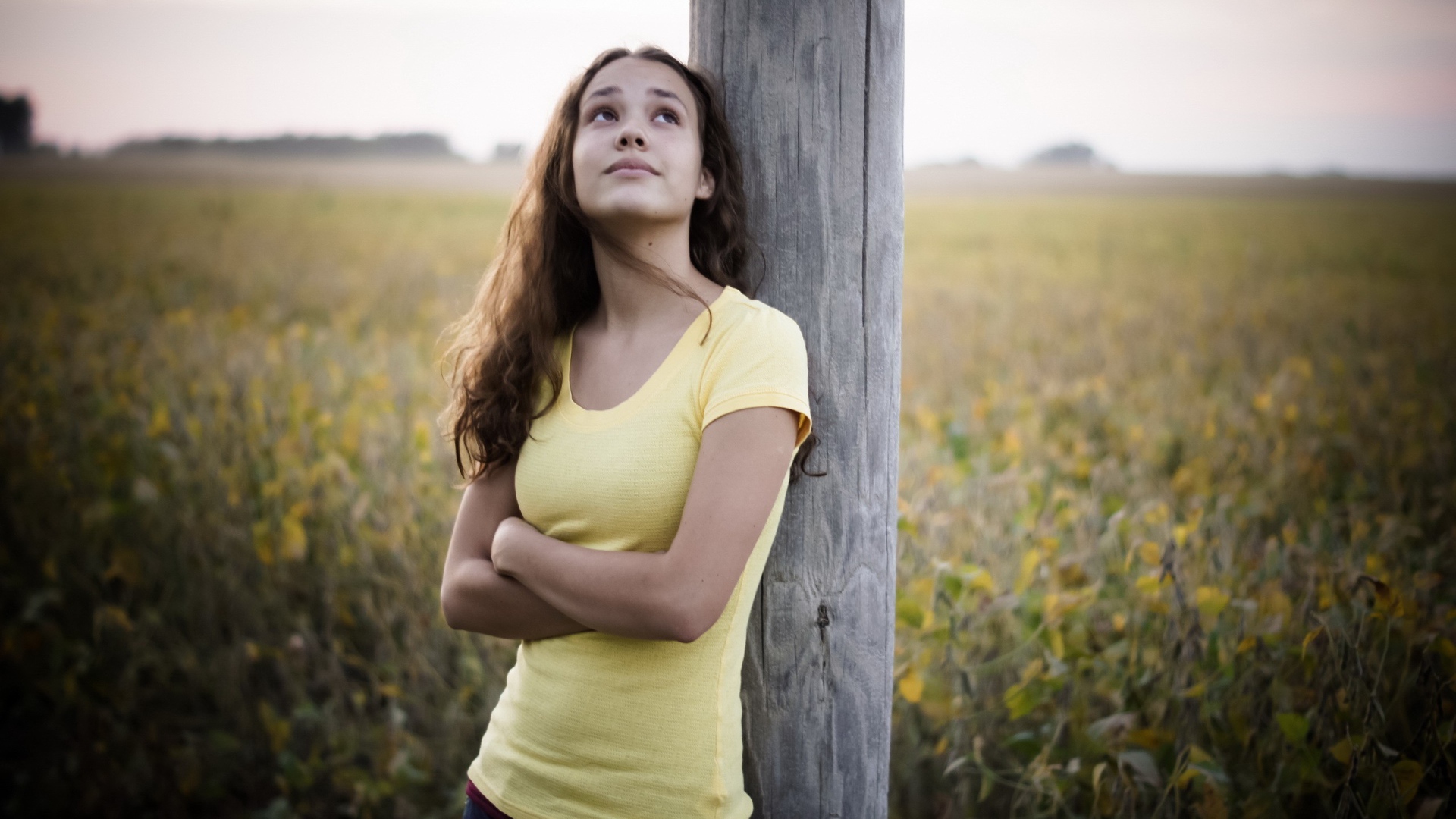 Девушка в желтой майке стоит у столба