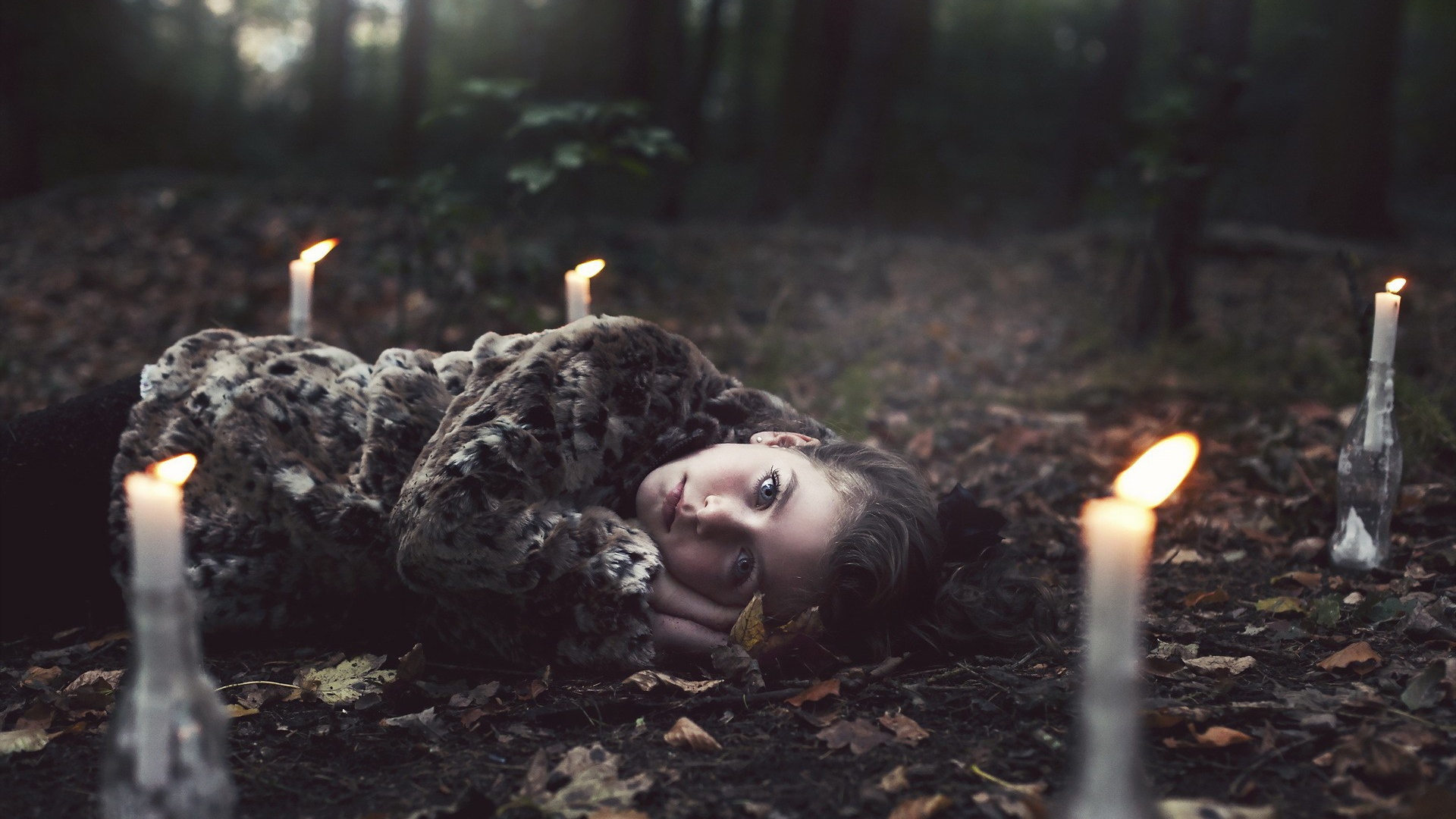 Девушка лежит среди свечей в лесу