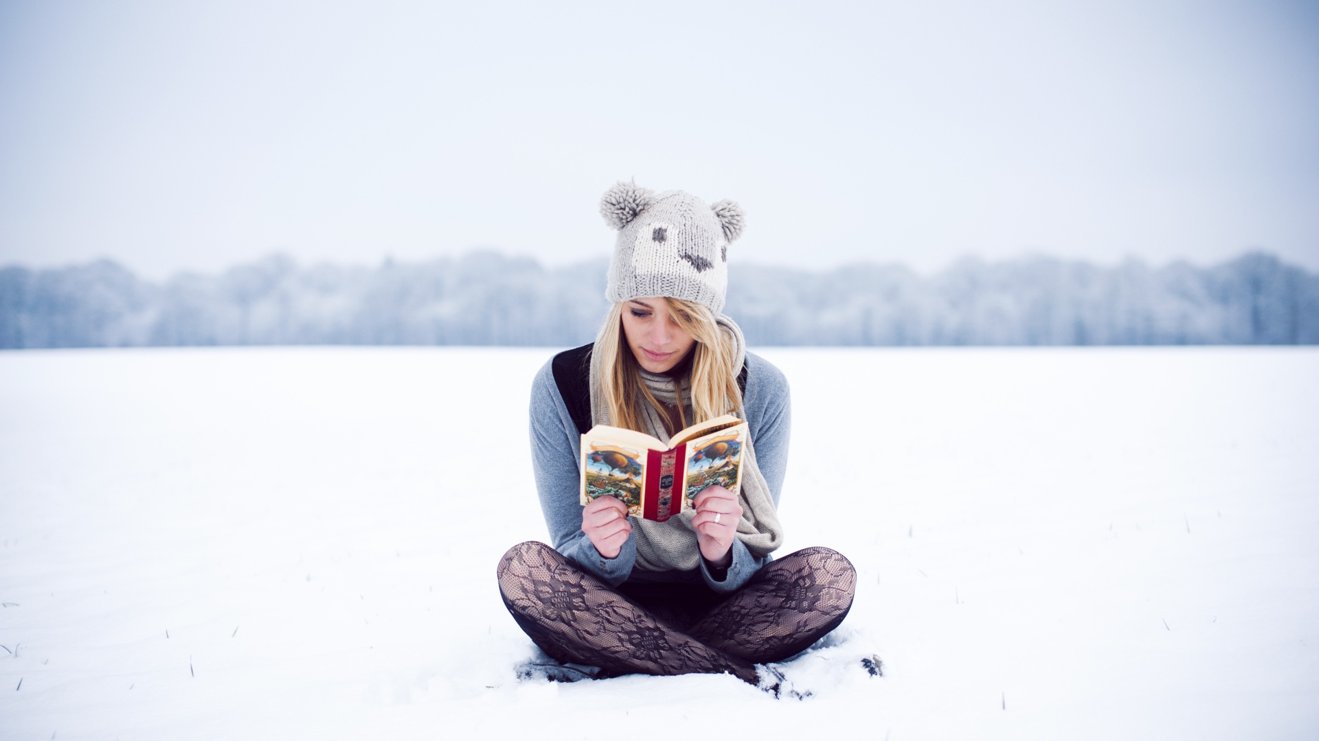 Девушка читает книгу сидя на снегу