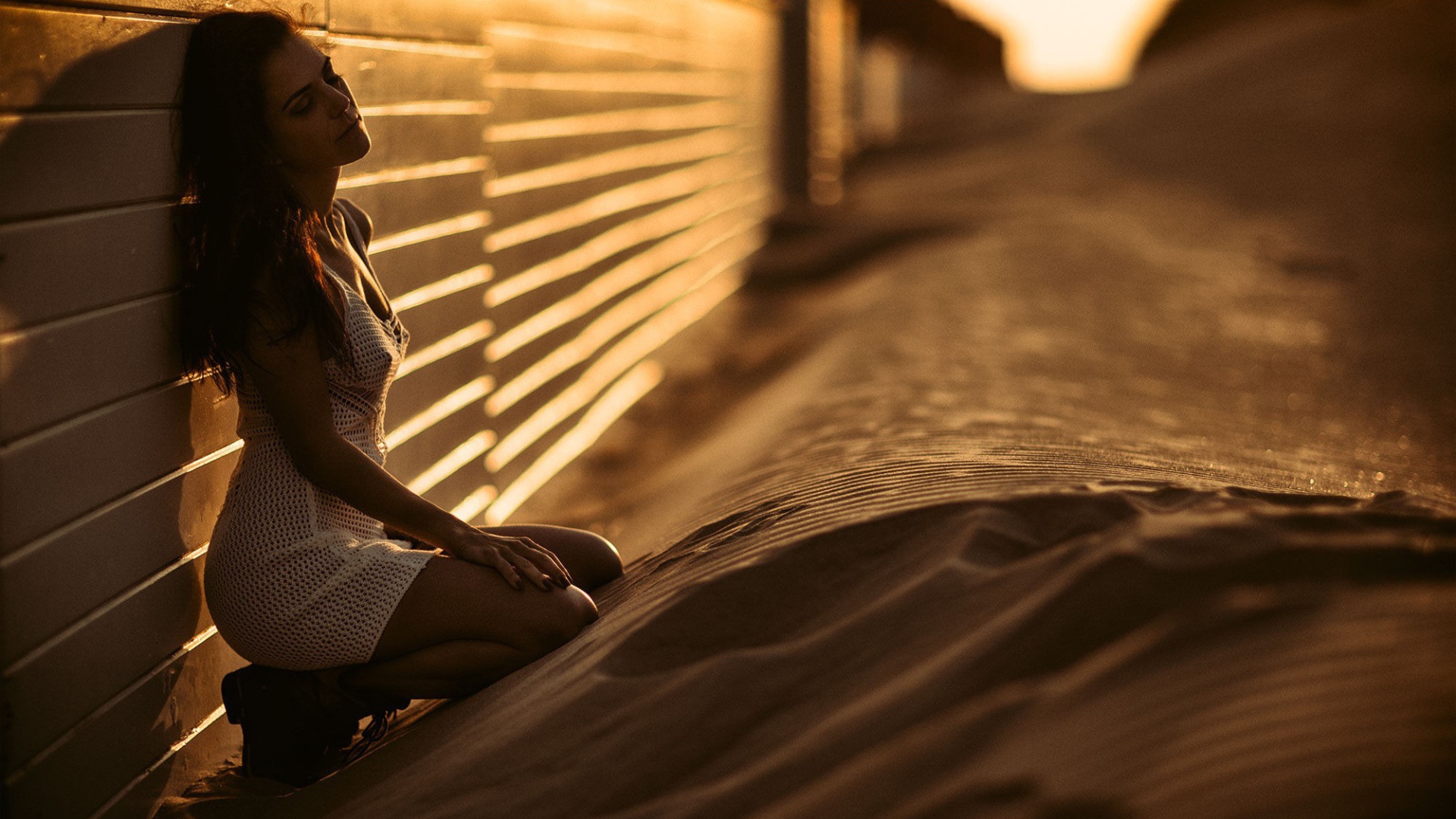 Девушка сидит на песке у забора