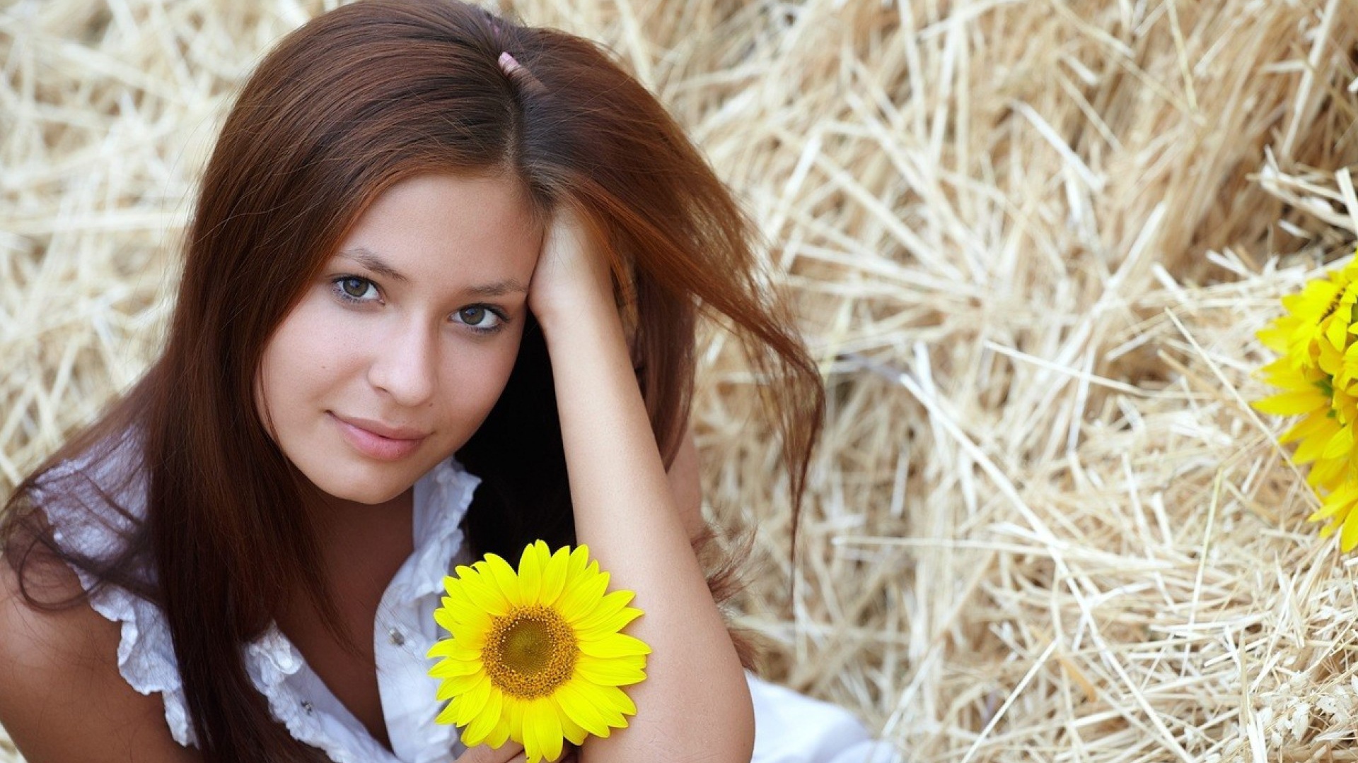 Девушка с желтым цветком сидит на сене