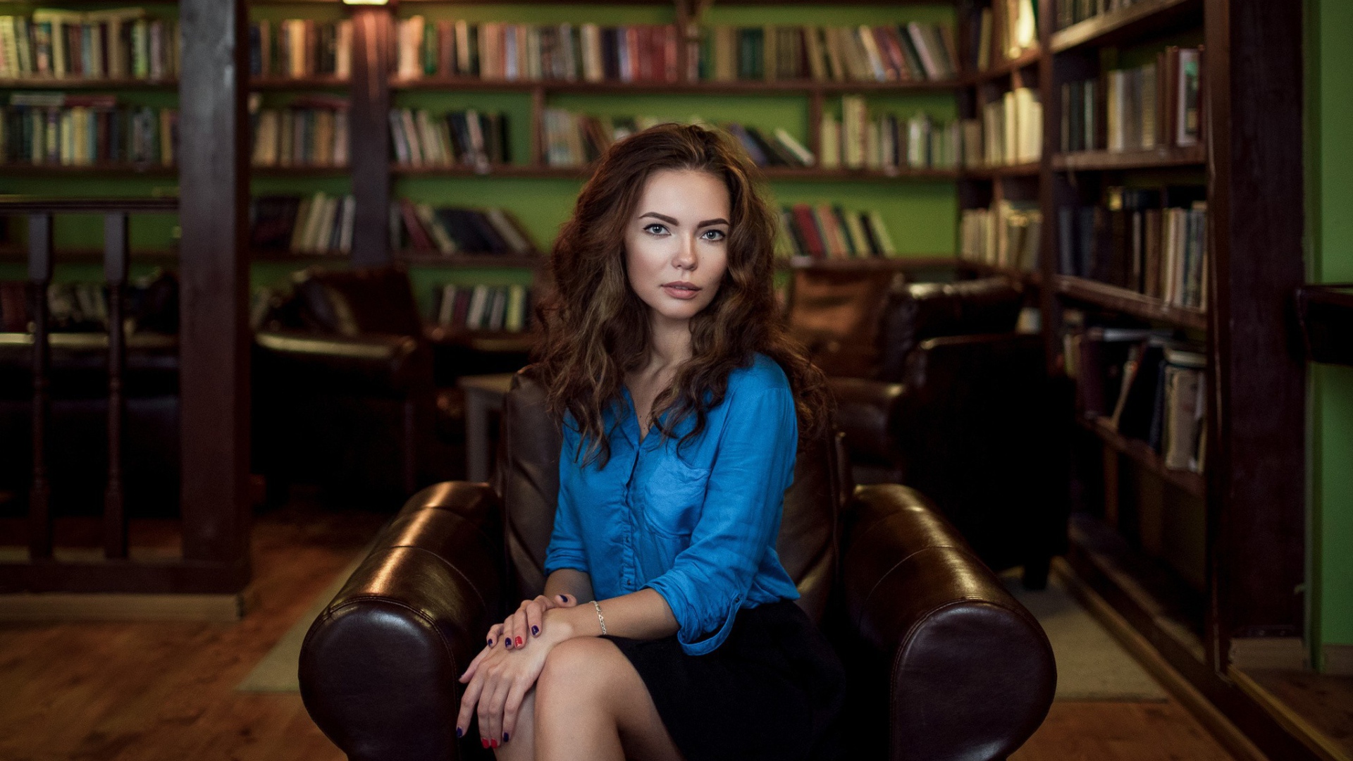Модель в голубой блузке сидит на кожаном кресле