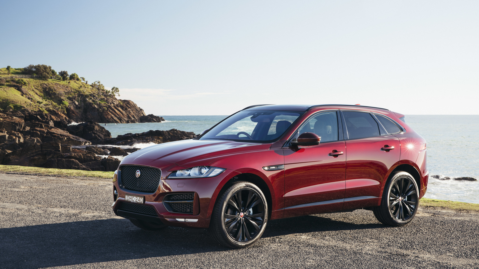 Бордовый автомобиль Jaguar F-Pace на фоне океана