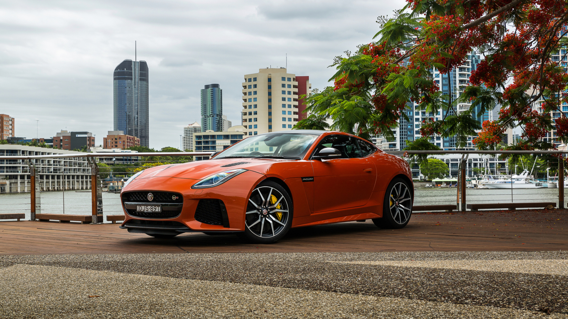 Оранжевый автомобиль Jaguar F-Type на фоне небоскребов 