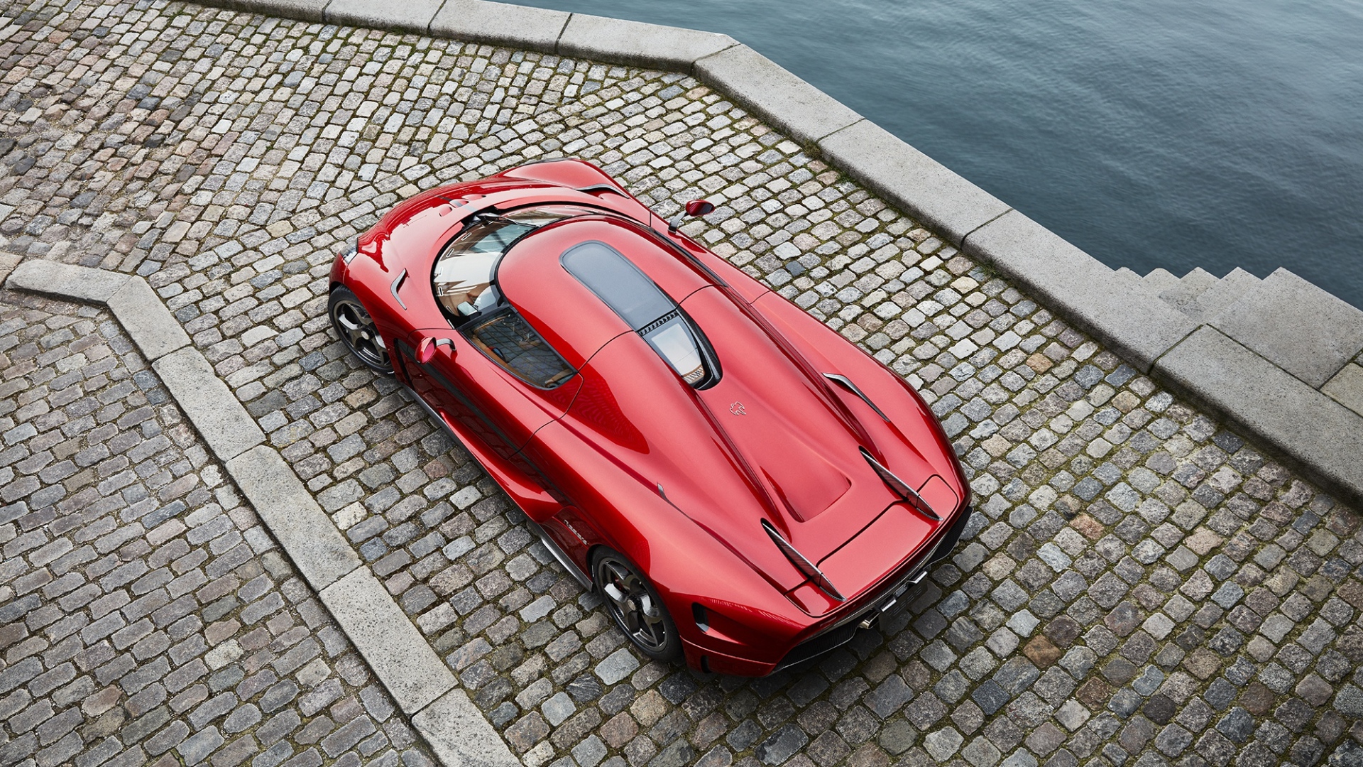 Красный спортивный автомобиль Koenigsegg Regera у воды, вид сверху
