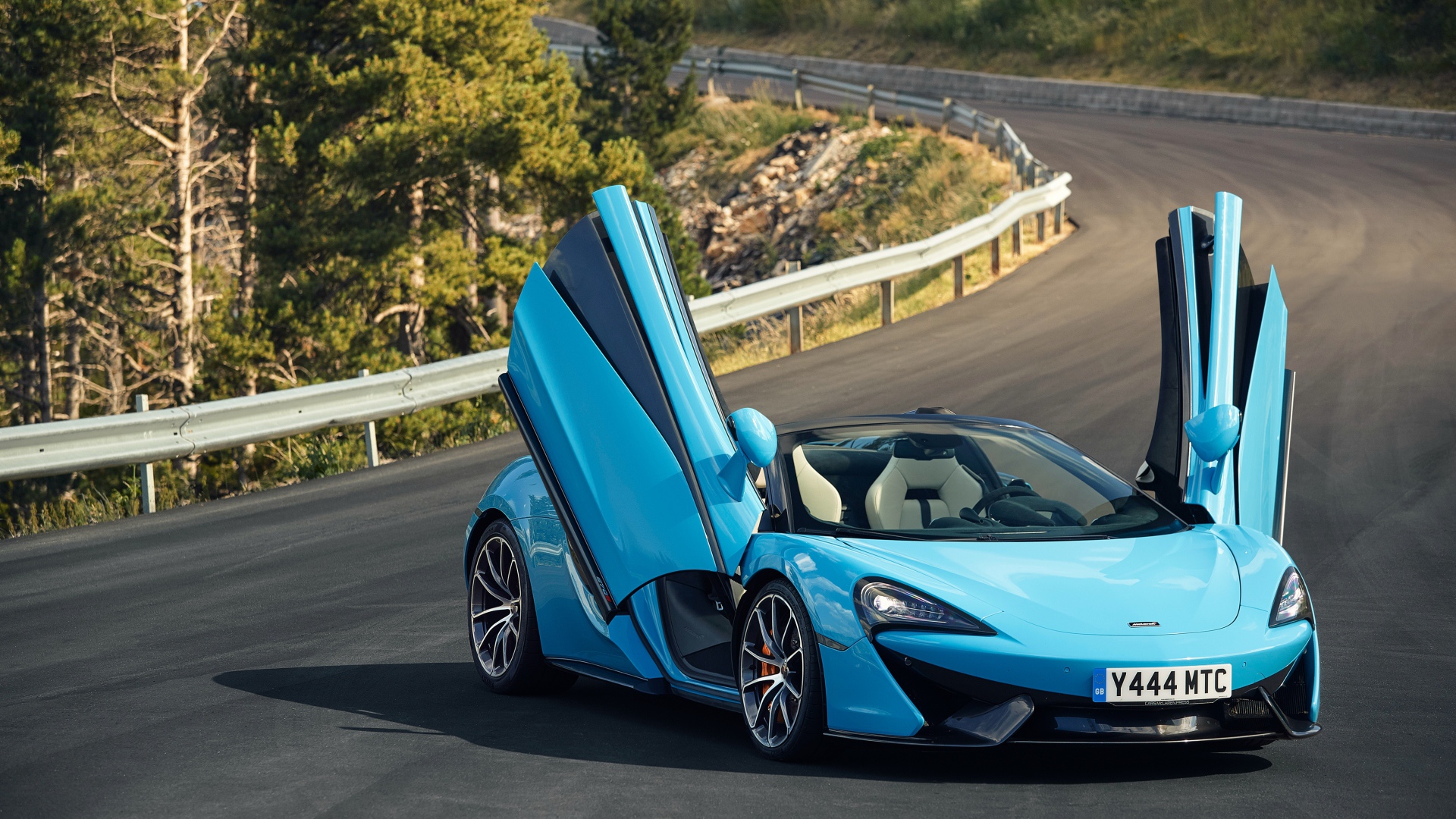 Синий спортивный автомобиль McLaren 570S на трассе с открытыми дверями