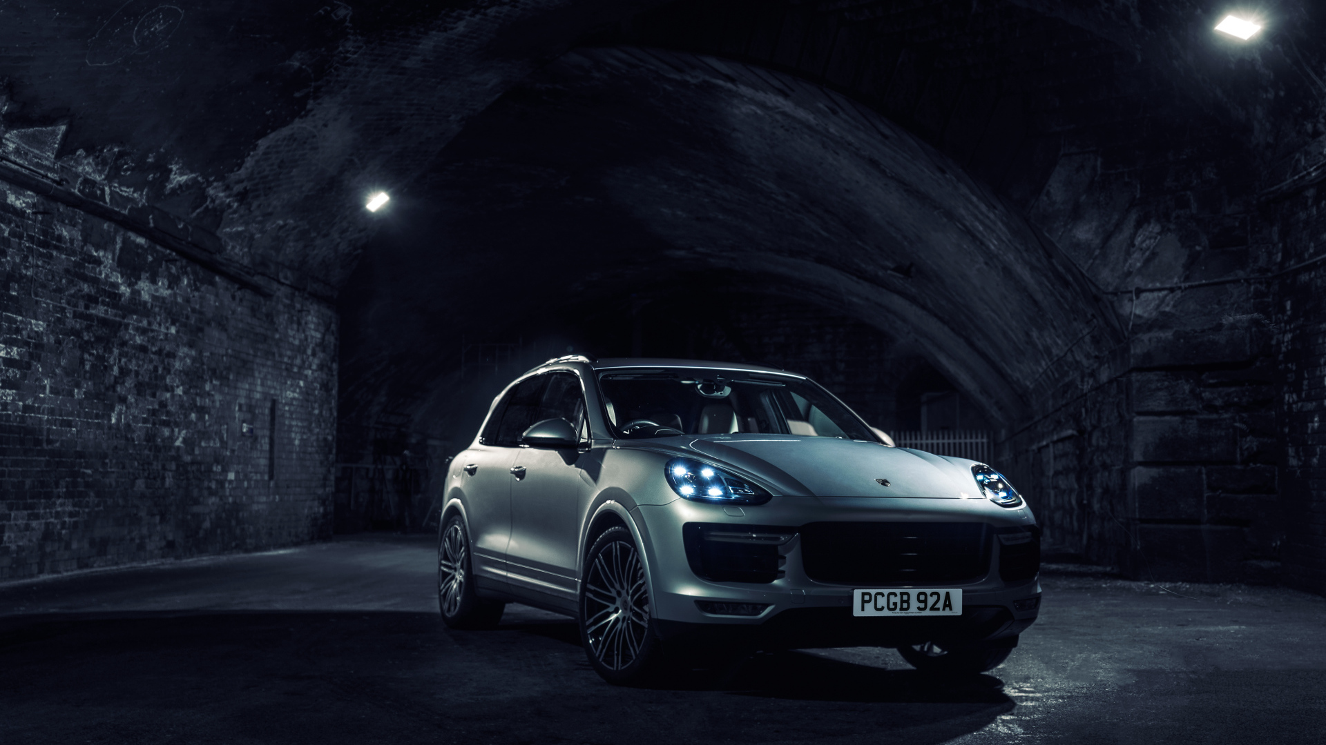 Серебристый автомобиль Porsche Cayenne в тоннеле с включенными фарами