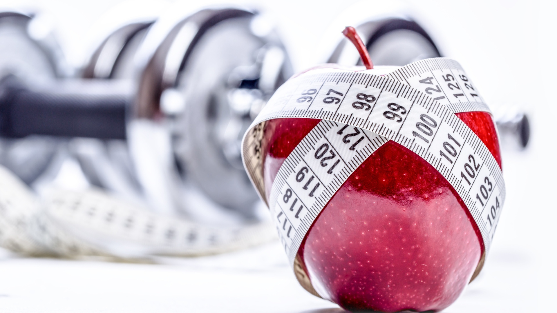 Красное яблоко перемотано мерной лентой и гантели на белом фоне