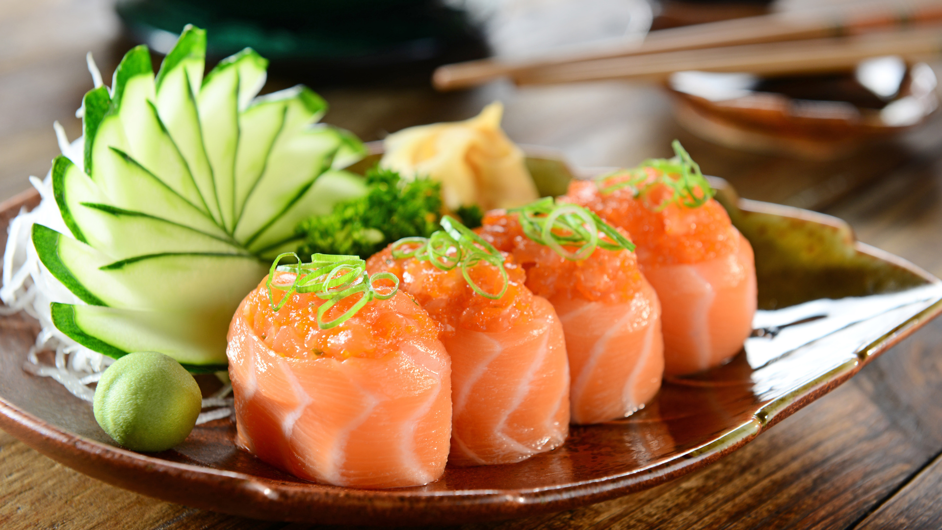 Суши из красной рыбы на тарелке со свежими огурцами и зеленью