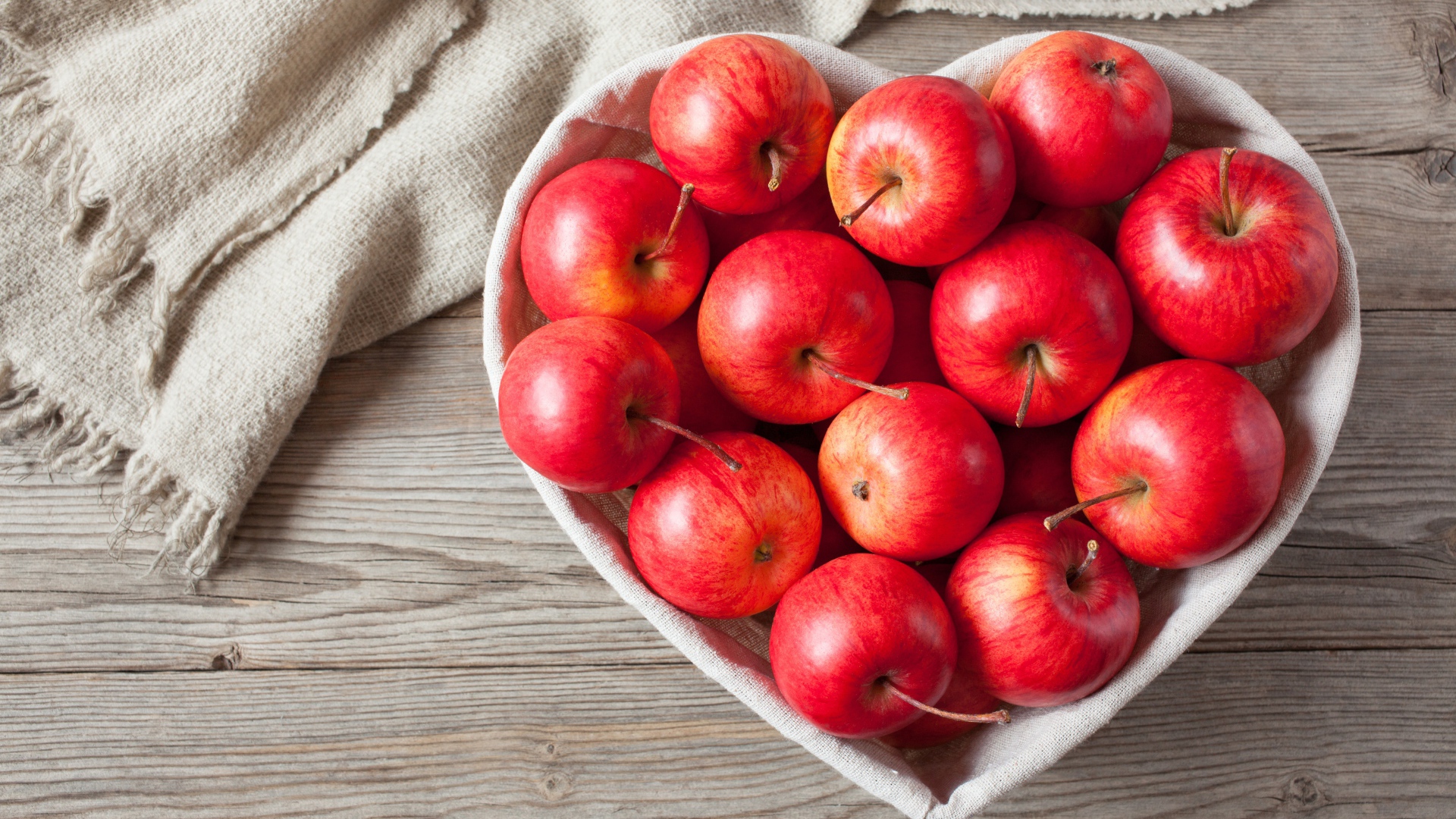 Красивые красные яблоки в тарелке в форме сердца на столе