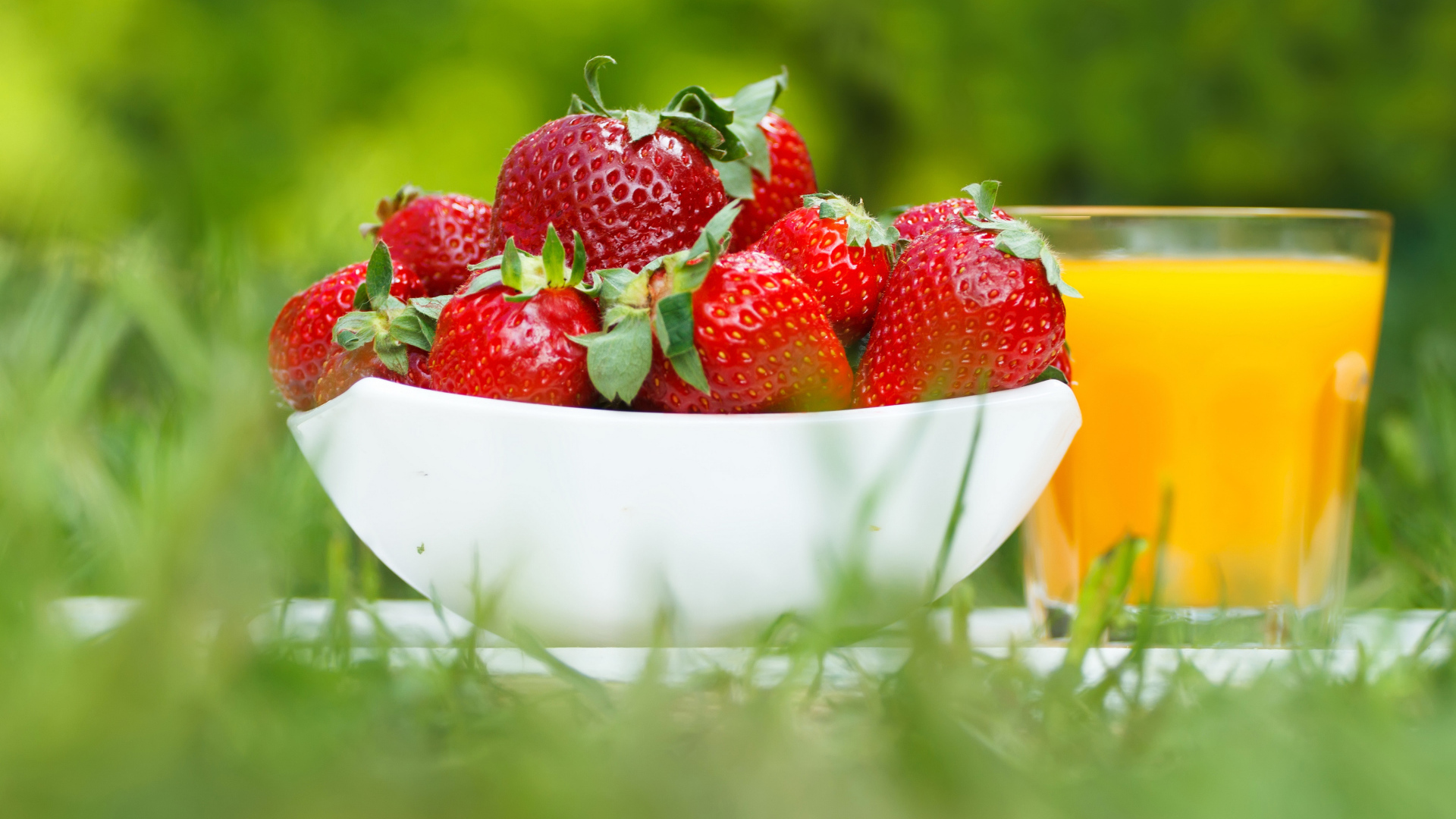 Спелые ягоды клубники и стакан апельсинового сока на зеленой траве