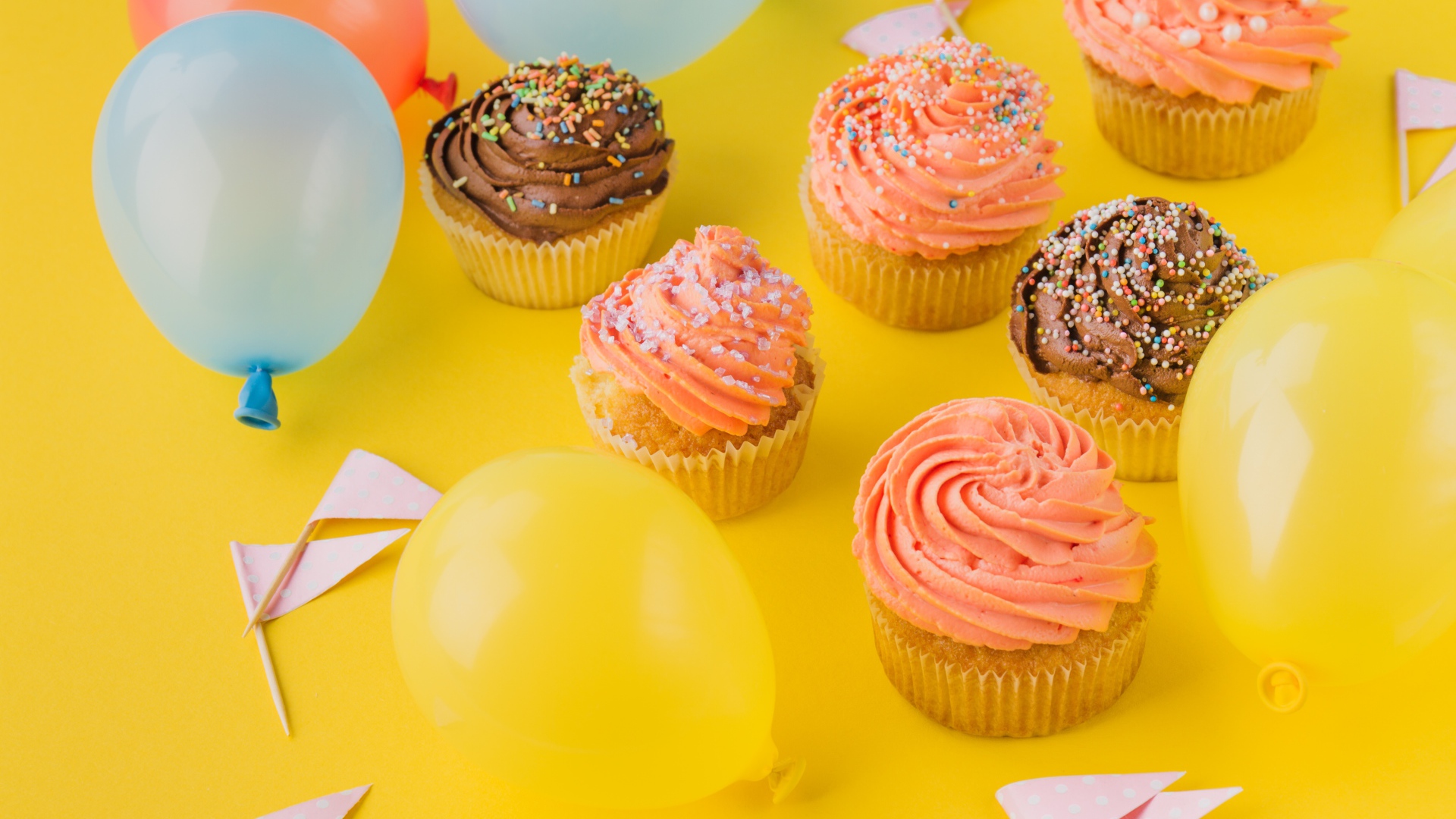 Аппетитные капкейки с кремом и воздушными шариками на желтой поверхности