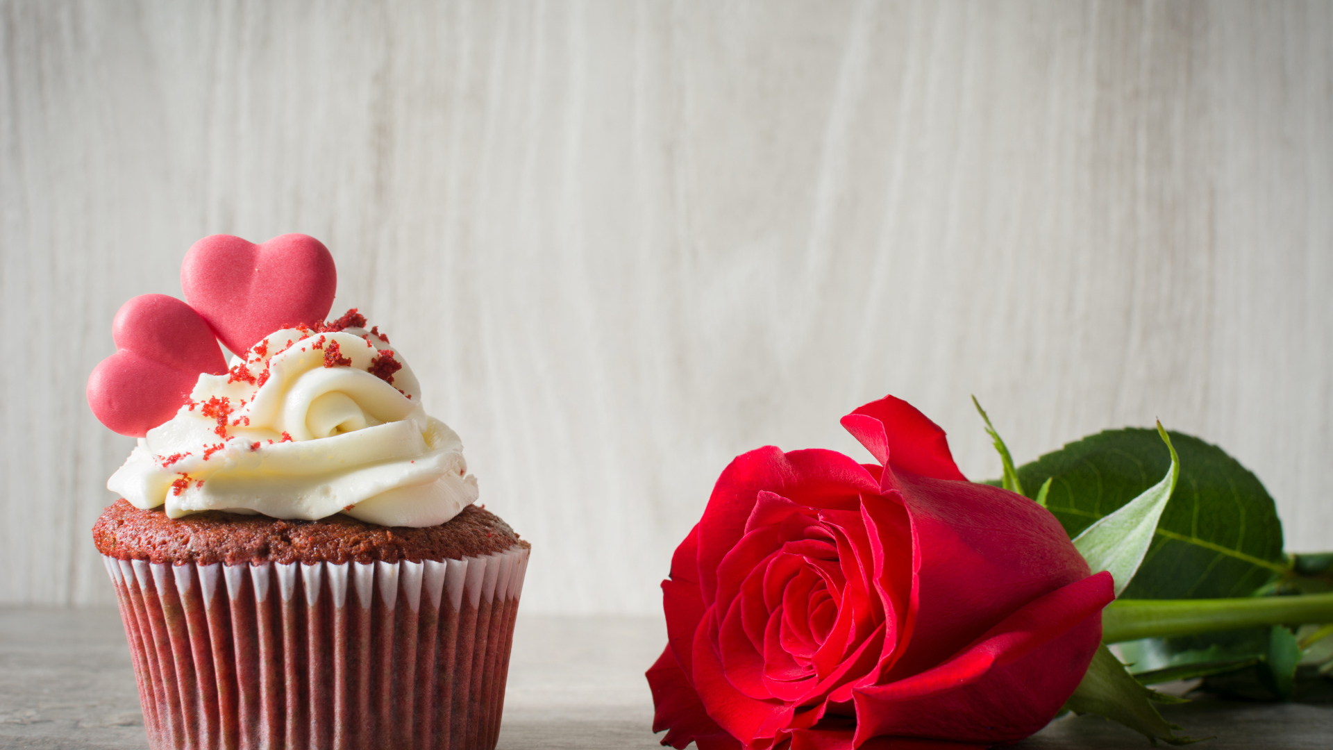 Капкейк с кремом и красной розой на столе