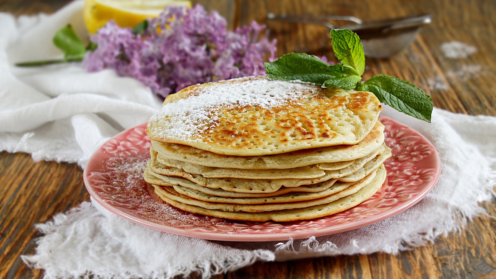 Тонкие блинчики на тарелке с сахарной пудрой и веточкой мяты