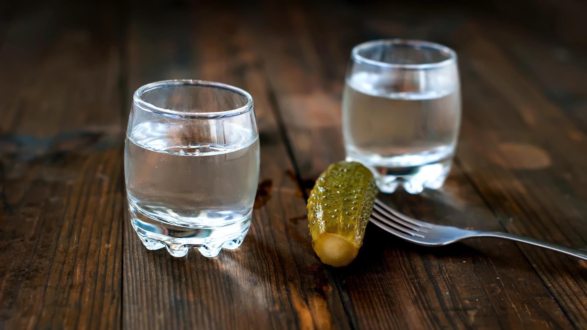Две рюмки водки и соленый огурец на столе
