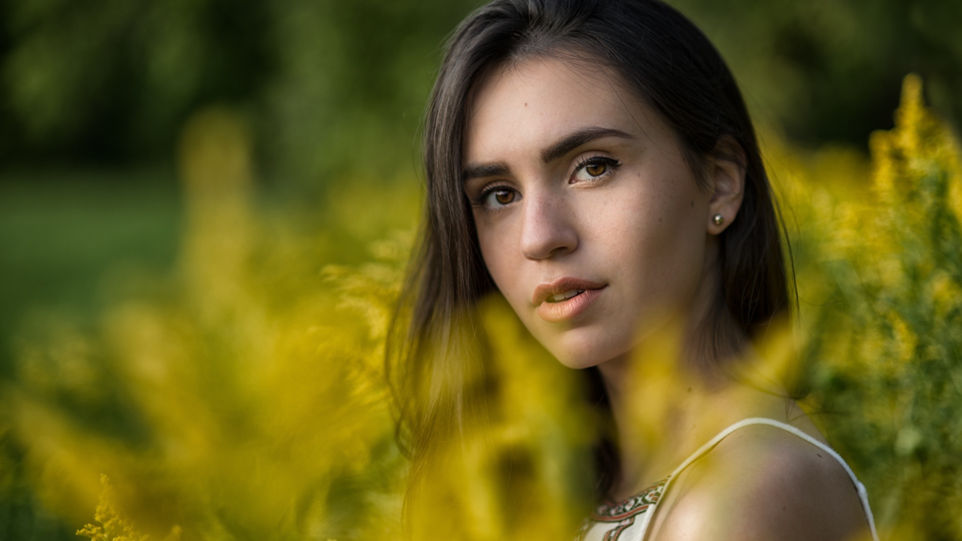 Красивая девушка с нежным взглядом сидит у желтых цветов