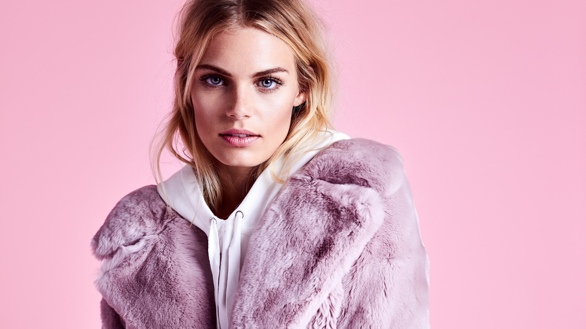 Красивая голубоглазая девушка в шубе на розовом фоне