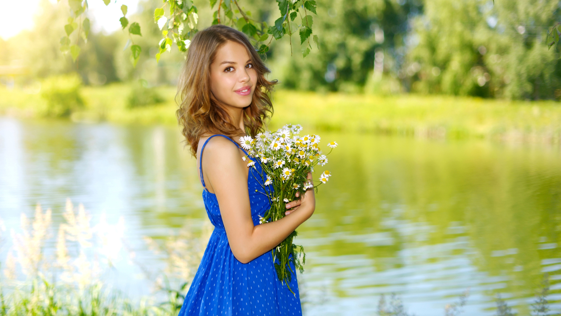 Красивая девушка шатенка в синем сарафане с букетом ромашек у воды