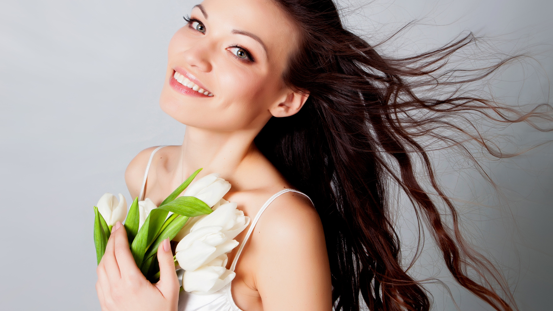 Красивая улыбающаяся брюнетка с букетом тюльпанов на сером фоне
