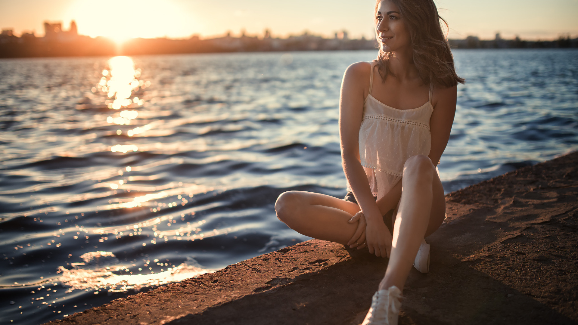 Красивая улыбающаяся девушка сидит в лучах солнца у реки