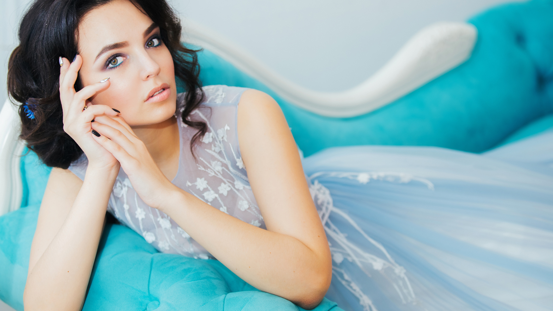 Девушка брюнетка в красивом платье лежит на голубом диване