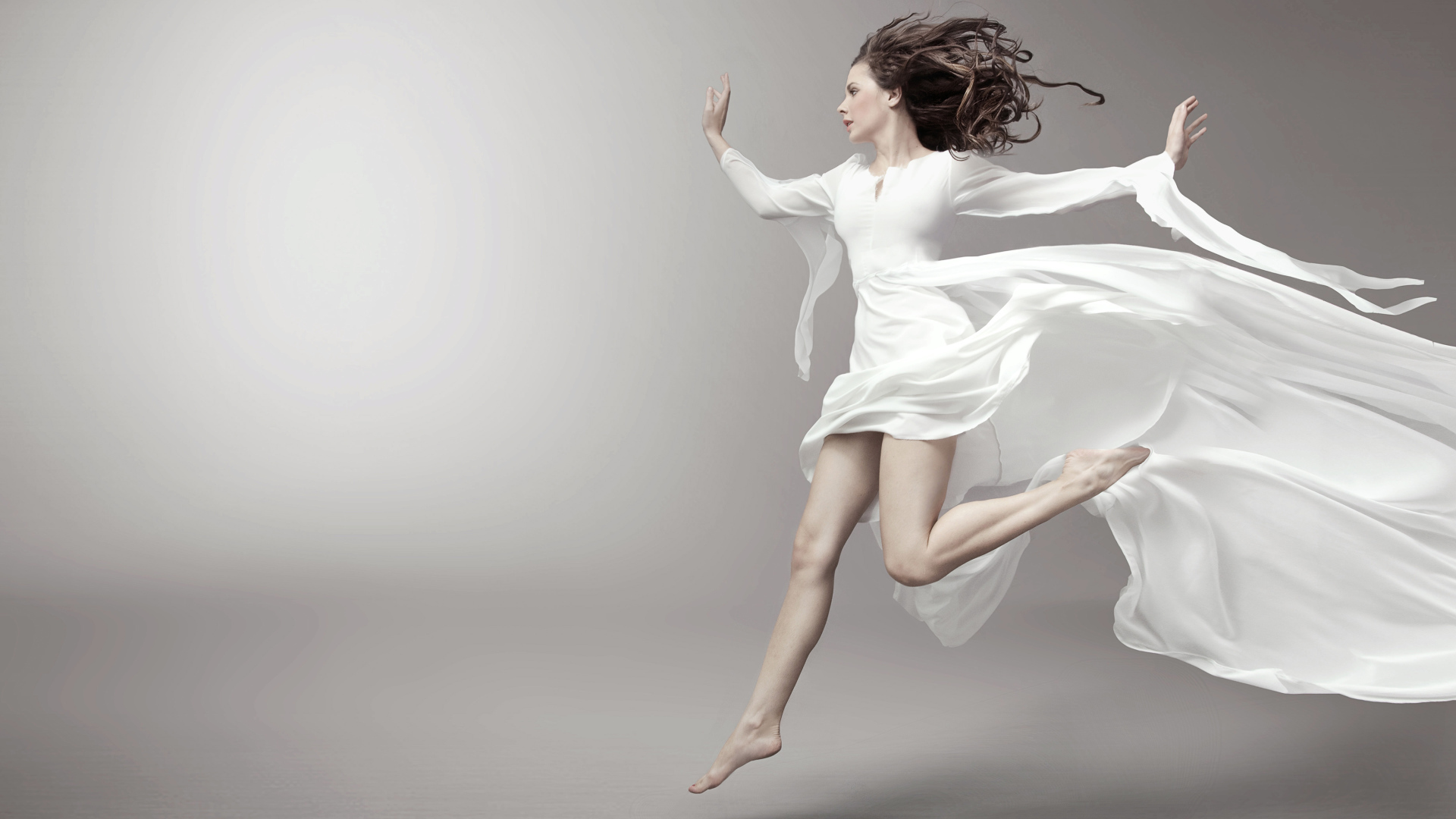 Бегущая красивая девушка в белом платье на сером фоне