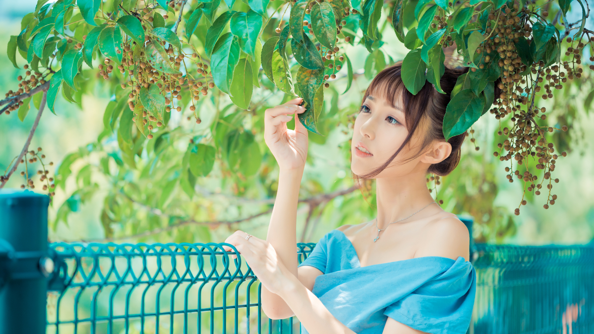 Молодая красивая девушка азиатка стоит у ветки с зелеными листьями