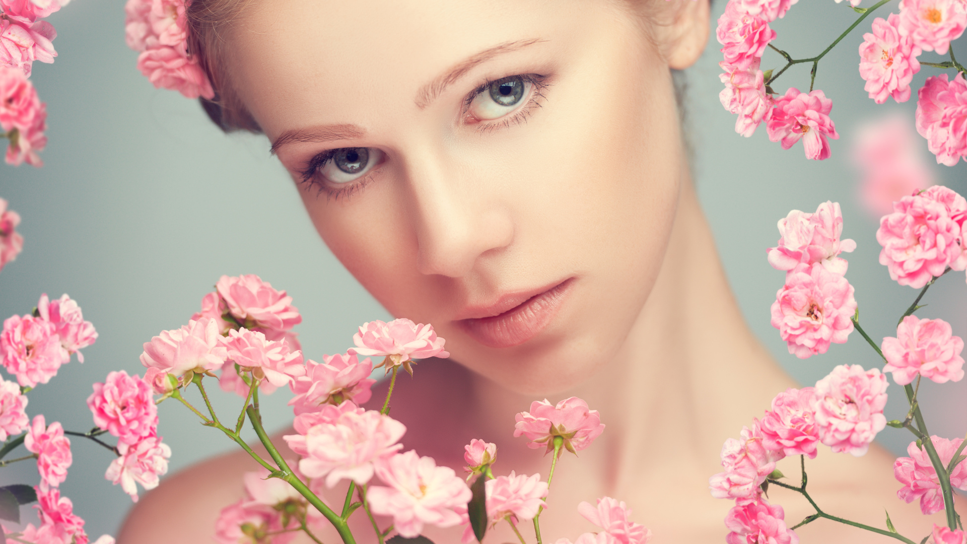 Молодая нежная девушка с розовыми розами на сером фоне