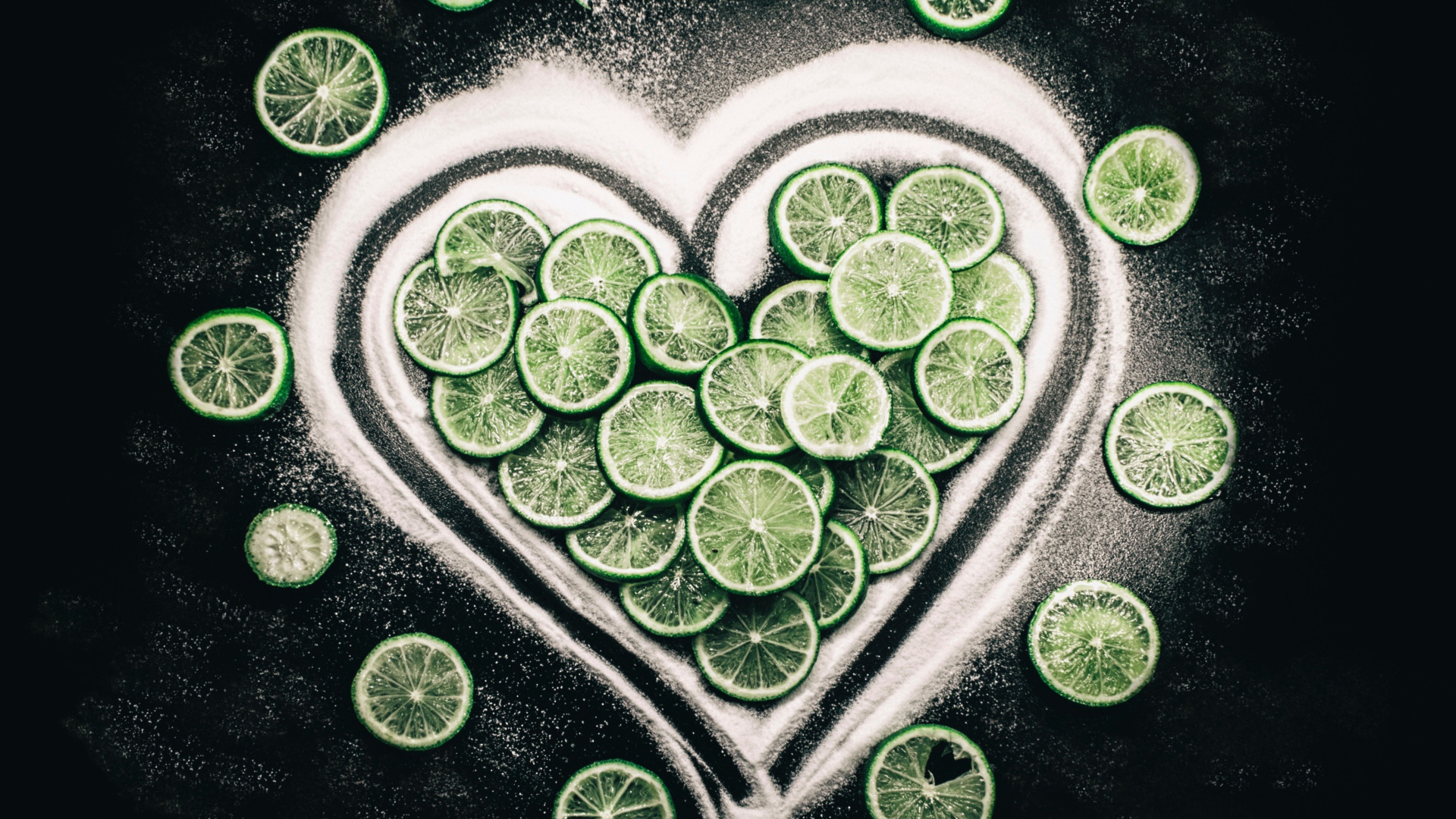Сердце из сахара и кружочков  зеленого лайма на черном фоне