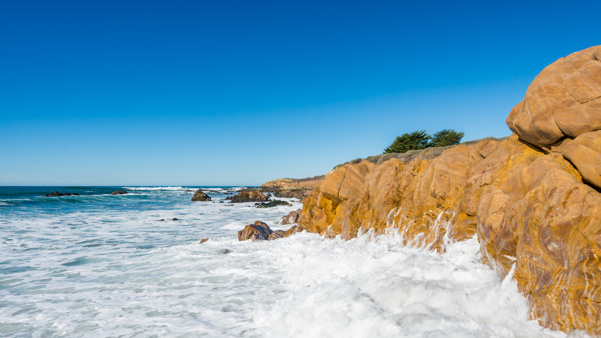 Белые волны бьются о скалы на берегу океана под голубым небом
