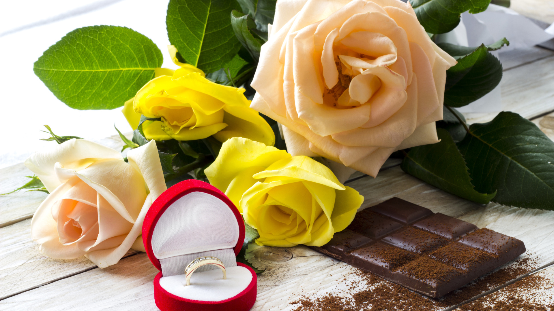 Букет роз на столе с шоколадкой и красной коробочкой с обручальным кольцом