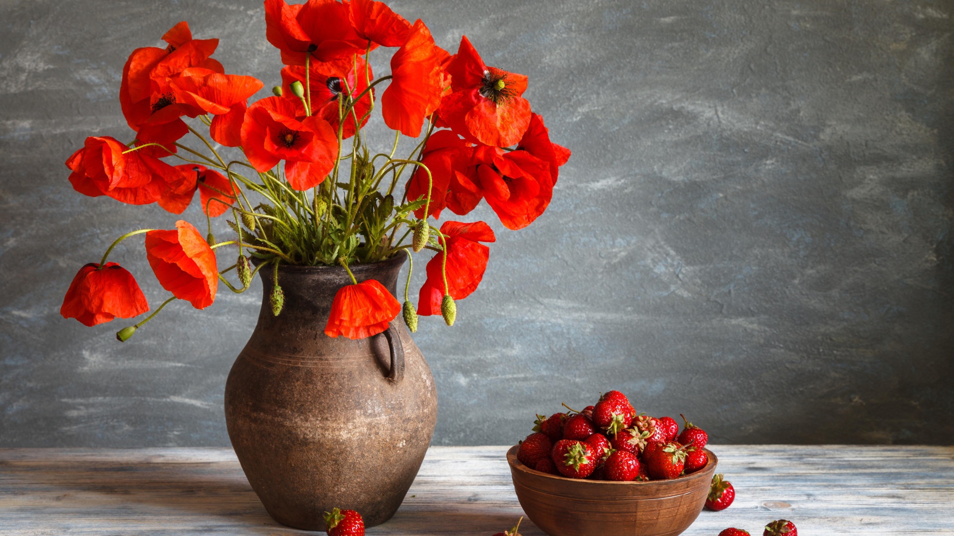 Красивый букет красных полевых маков в вазе на столе с клубникой