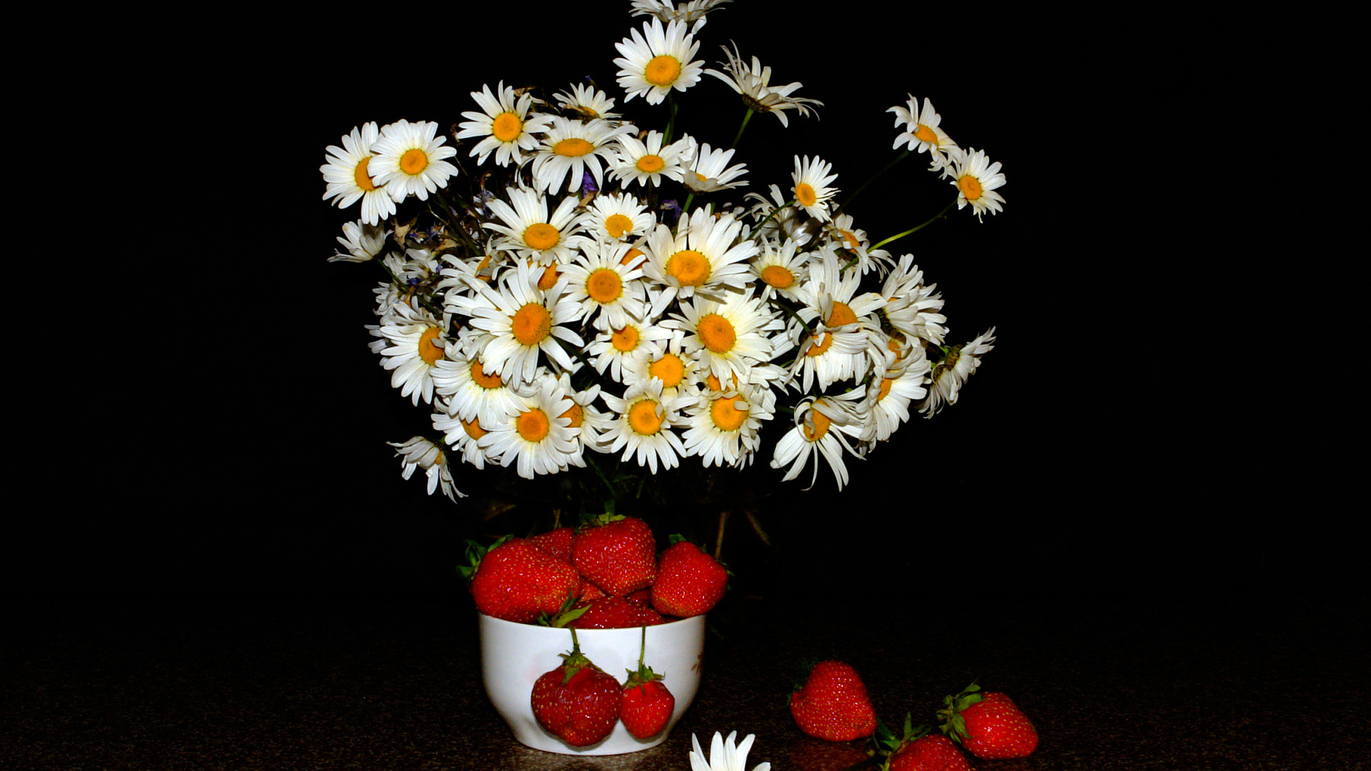 Белые полевые ромашки и клубника на столе на черном фоне