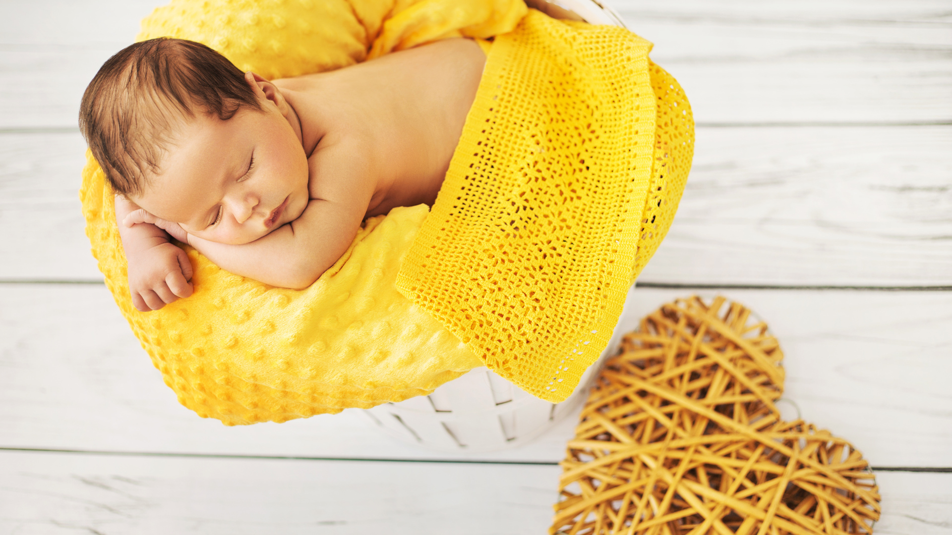 Грудной ребенок спит на желтой подушке с плетеным сердцем