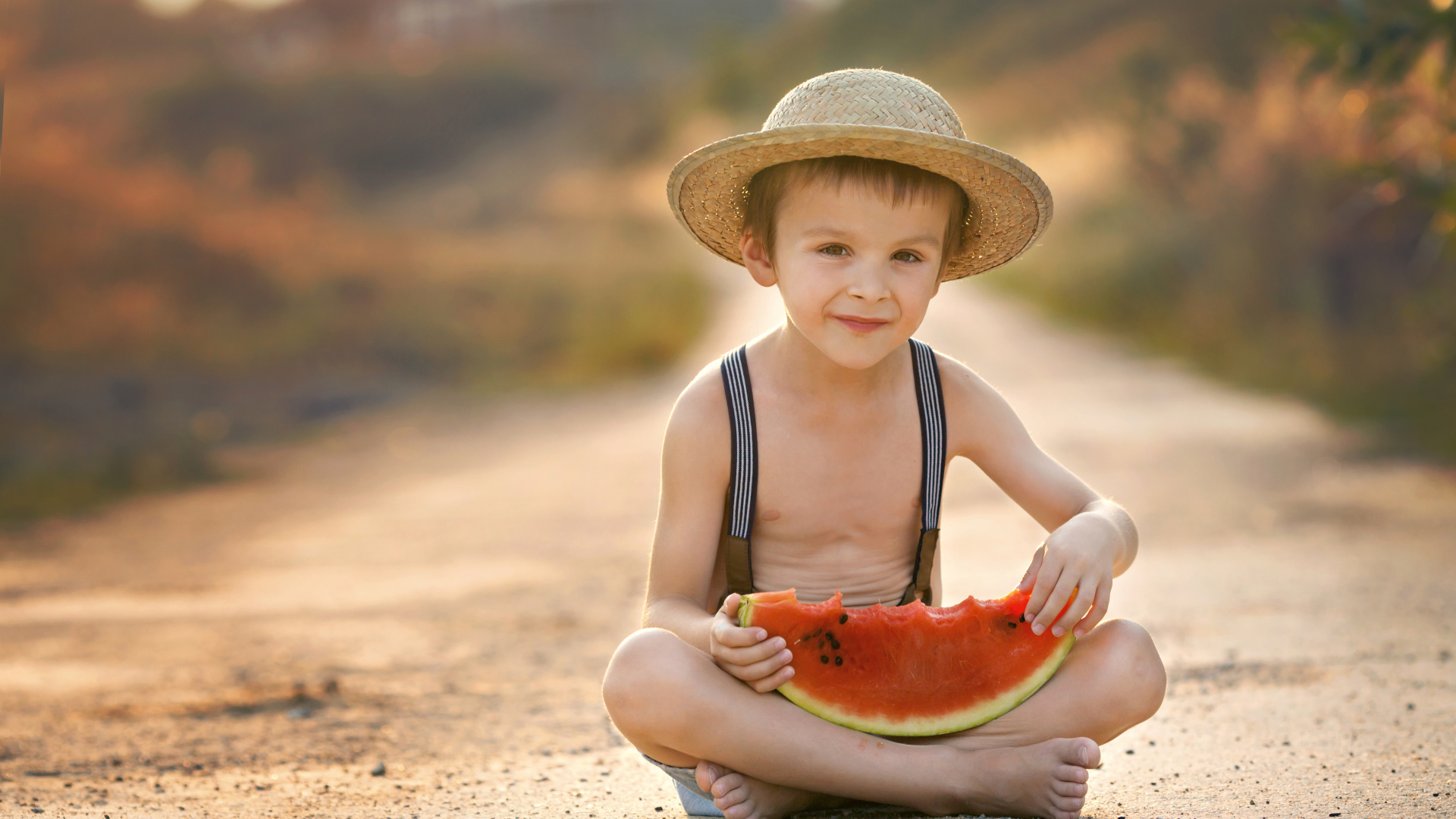 Маленький мальчик в шляпе сидит на дороге с долькой арбуза