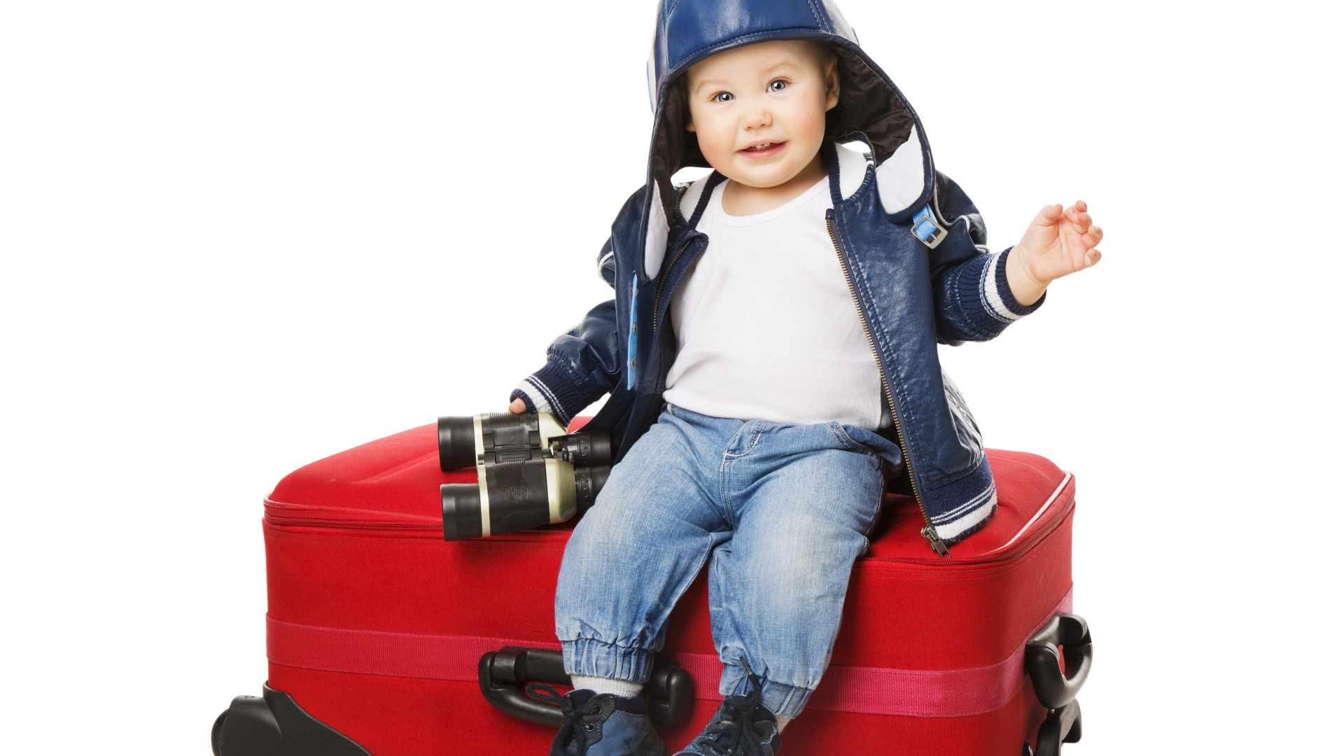 Маленький мальчик в шапке с биноклем сидит на красном чемодане